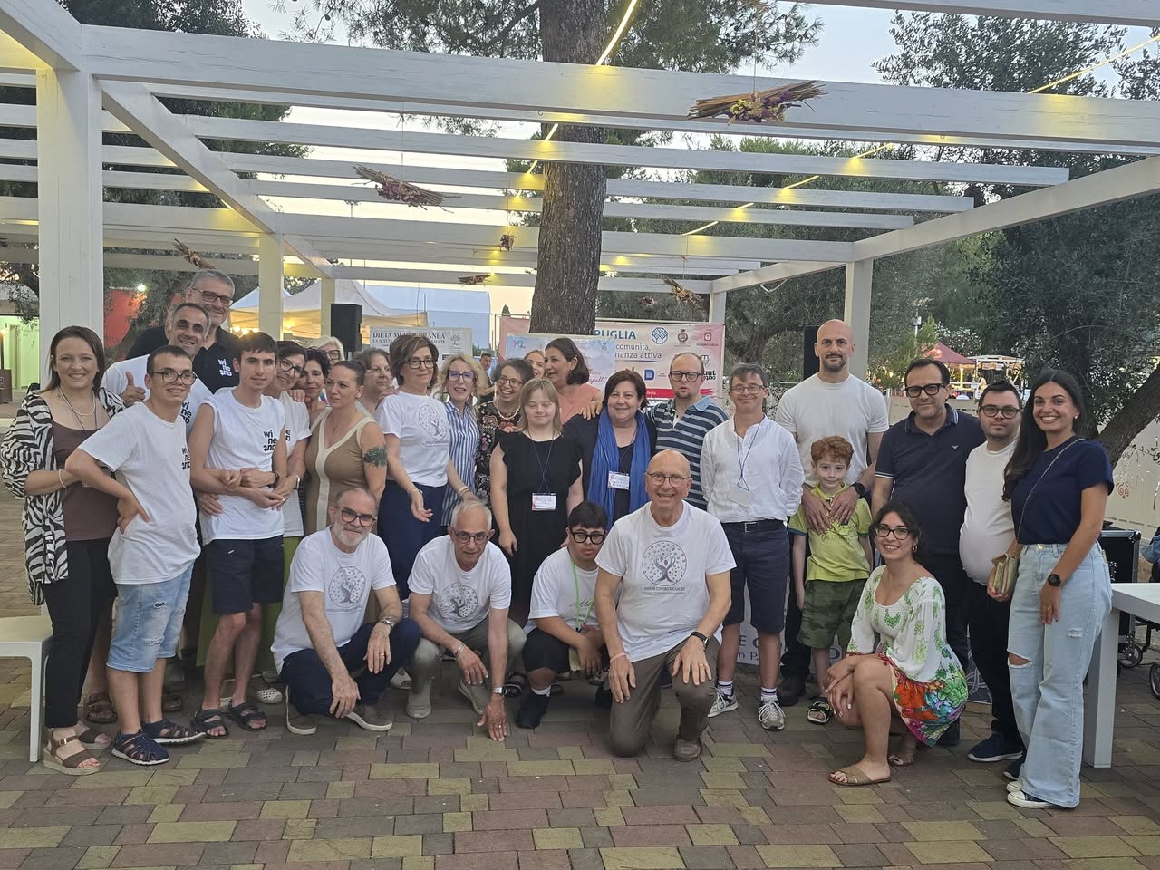 Foto di gruppo di volontari e partner dei presidi sotto la pergola dei Giardini Forum Eventi