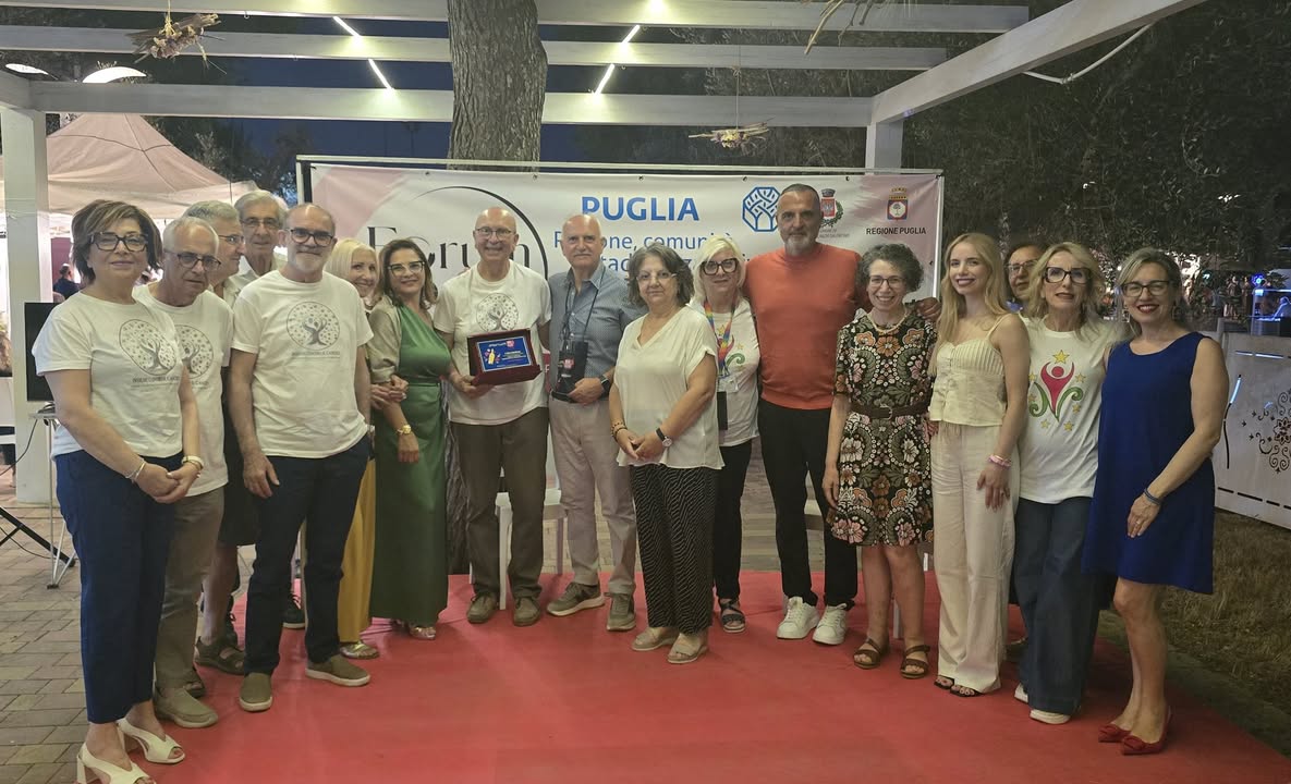 Foto di gruppo della serata conclusiva con la targa, davanti al banner di Forum Aperto