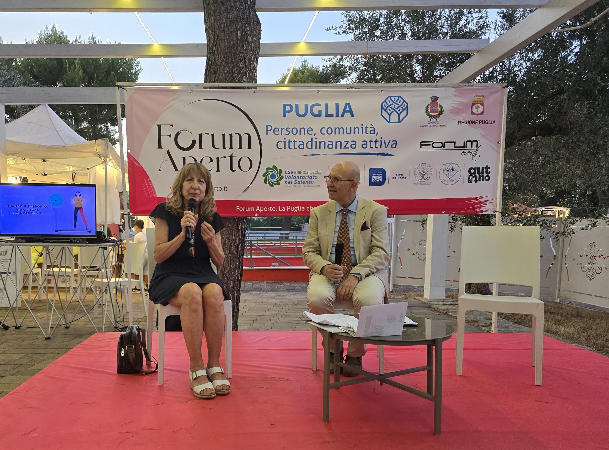 La dott.ssa Lucia Valente al microfono durante l'incontro sulla nutrizione, con lo schermo delle infografiche del presidio salute